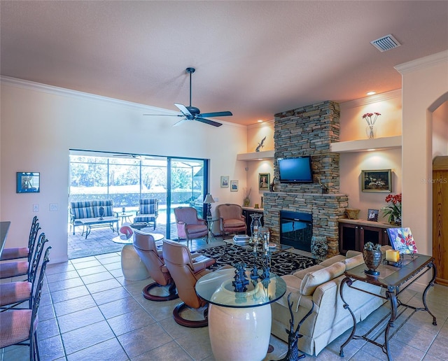 tiled living room featuring a stone fireplace, ceiling fan, and ornamental molding