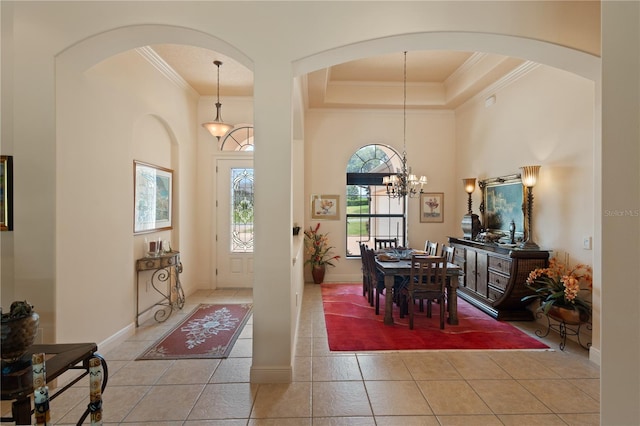 tiled entrance foyer featuring a tray ceiling, crown molding, a chandelier, and a high ceiling