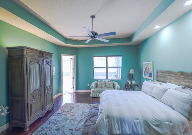 bedroom with a raised ceiling, ceiling fan, a textured ceiling, and dark hardwood / wood-style floors