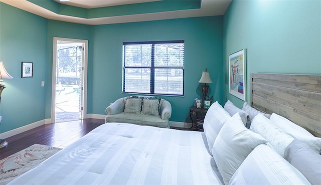 bedroom featuring dark hardwood / wood-style flooring, access to outside, and a raised ceiling