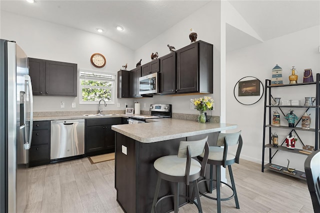 kitchen featuring appliances with stainless steel finishes, kitchen peninsula, vaulted ceiling, and light hardwood / wood-style floors