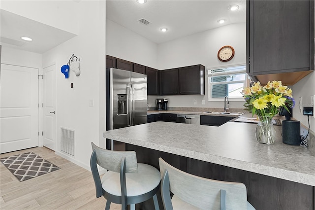 kitchen with light wood-type flooring, appliances with stainless steel finishes, sink, a kitchen bar, and kitchen peninsula