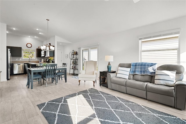 living room featuring sink, light hardwood / wood-style flooring, vaulted ceiling, and an inviting chandelier