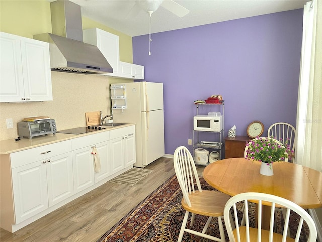 kitchen with ceiling fan, white cabinetry, wall chimney range hood, light wood-type flooring, and white appliances