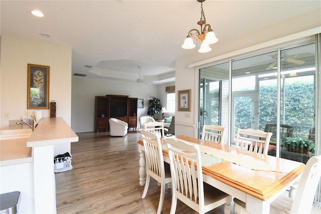 dining space featuring wood-type flooring, ceiling fan with notable chandelier, and a tray ceiling