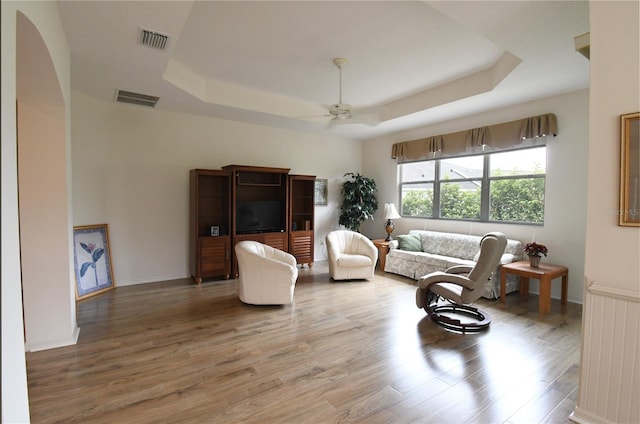 living room with hardwood / wood-style floors, ceiling fan, and a raised ceiling