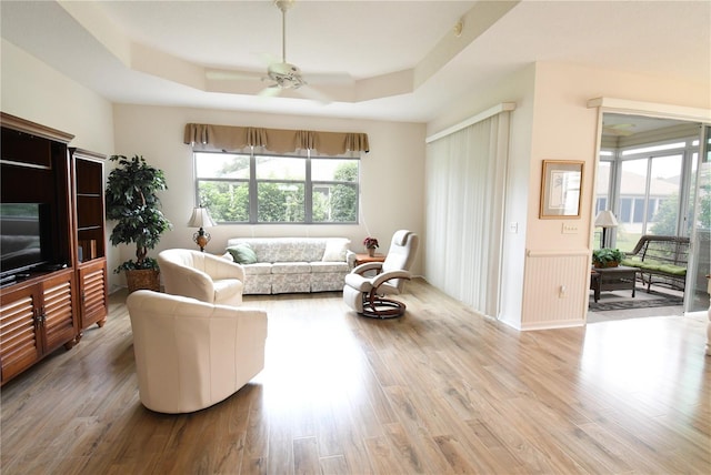 living room with ceiling fan, a wealth of natural light, wood-type flooring, and a raised ceiling