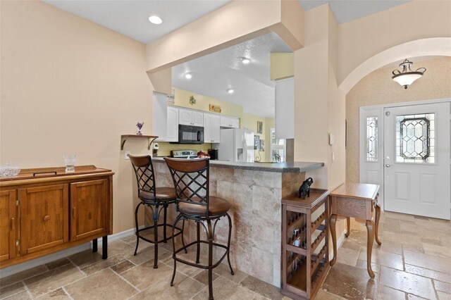 kitchen featuring a breakfast bar, white refrigerator with ice dispenser, kitchen peninsula, and white cabinets