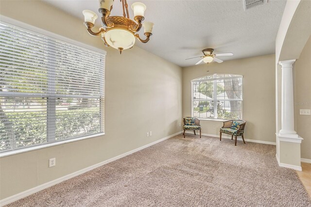 unfurnished room with a textured ceiling, ceiling fan with notable chandelier, decorative columns, and light colored carpet