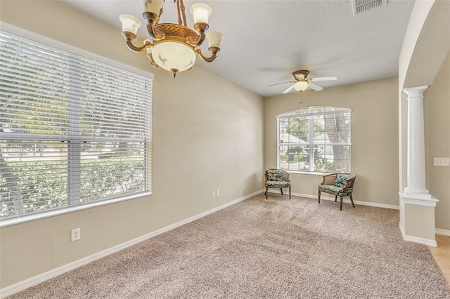 empty room featuring ceiling fan with notable chandelier, carpet floors, a textured ceiling, and ornate columns