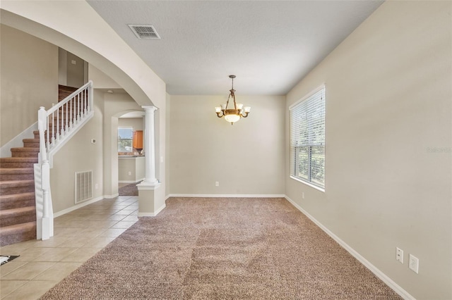 spare room with a notable chandelier, light tile patterned flooring, a textured ceiling, and ornate columns