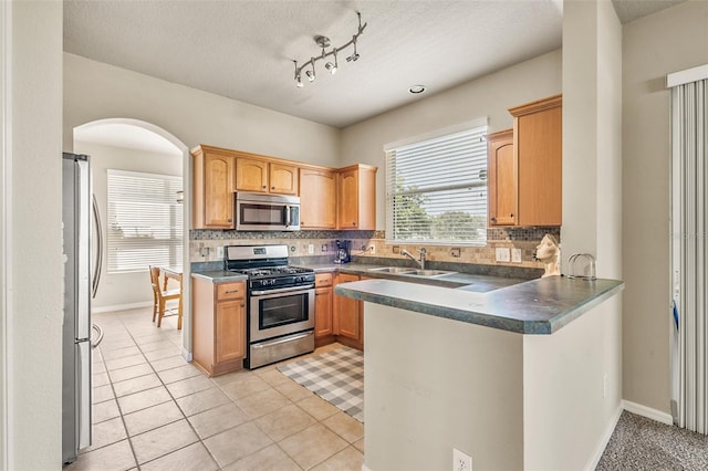 kitchen with sink, tasteful backsplash, a textured ceiling, light tile patterned floors, and stainless steel appliances