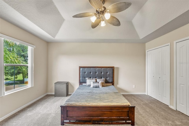 carpeted bedroom with ceiling fan, a raised ceiling, and two closets