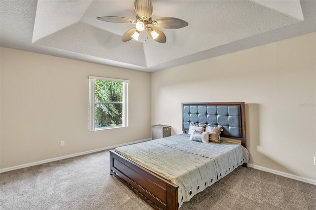 carpeted bedroom featuring a textured ceiling, ceiling fan, and a raised ceiling