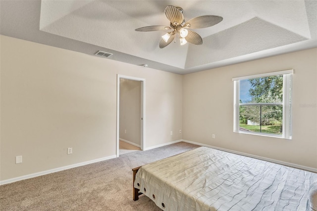 unfurnished bedroom featuring ceiling fan, light colored carpet, a textured ceiling, and a tray ceiling