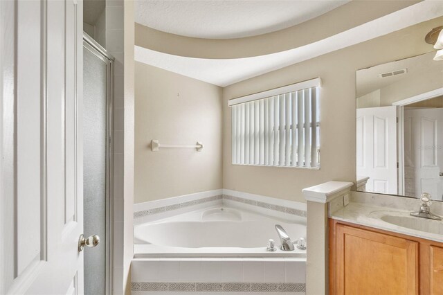 bathroom featuring a textured ceiling, tiled tub, and vanity