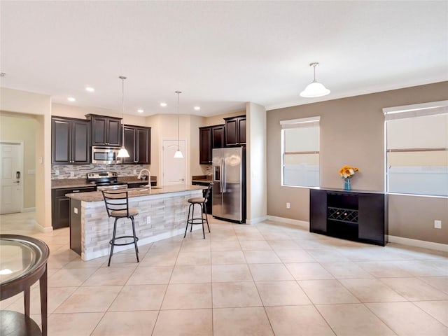 kitchen with decorative light fixtures, tasteful backsplash, an island with sink, a breakfast bar area, and appliances with stainless steel finishes