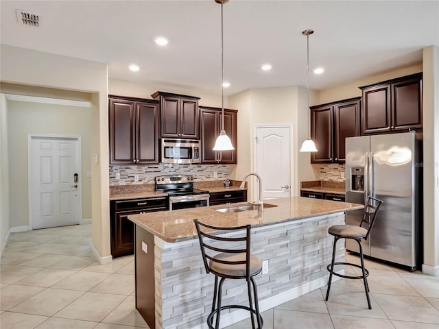 kitchen featuring decorative light fixtures, sink, a kitchen bar, light stone countertops, and appliances with stainless steel finishes