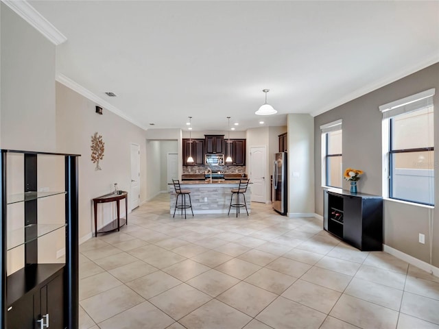 kitchen with a breakfast bar area, backsplash, appliances with stainless steel finishes, ornamental molding, and dark brown cabinets