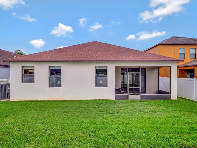 rear view of property featuring a shingled roof, a lawn, fence, and stucco siding