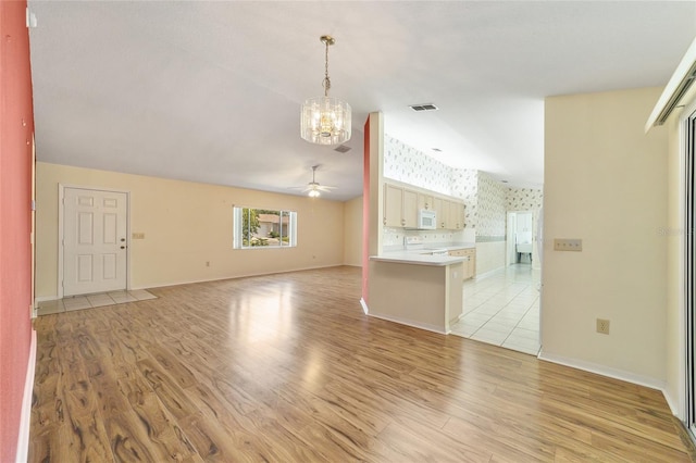 unfurnished living room with light wood-type flooring and ceiling fan with notable chandelier