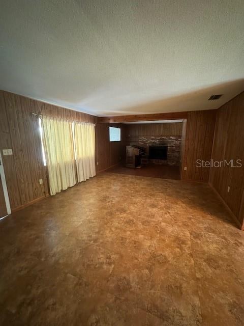 unfurnished living room with tile patterned floors, a fireplace, wood walls, and a textured ceiling