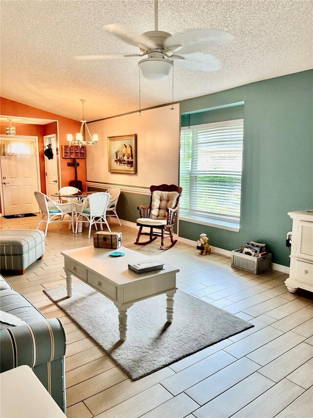 living room with ceiling fan with notable chandelier, a textured ceiling, light wood-type flooring, and vaulted ceiling