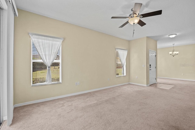 carpeted spare room featuring ceiling fan with notable chandelier