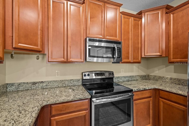 kitchen featuring appliances with stainless steel finishes, a textured ceiling, and light stone countertops