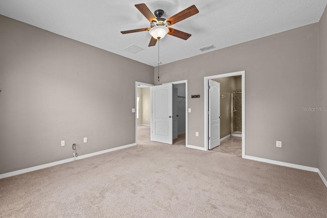 unfurnished bedroom featuring ceiling fan, ensuite bath, a walk in closet, and light colored carpet