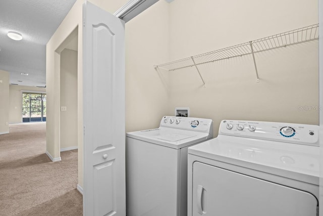 clothes washing area with a textured ceiling, light carpet, and washer and clothes dryer