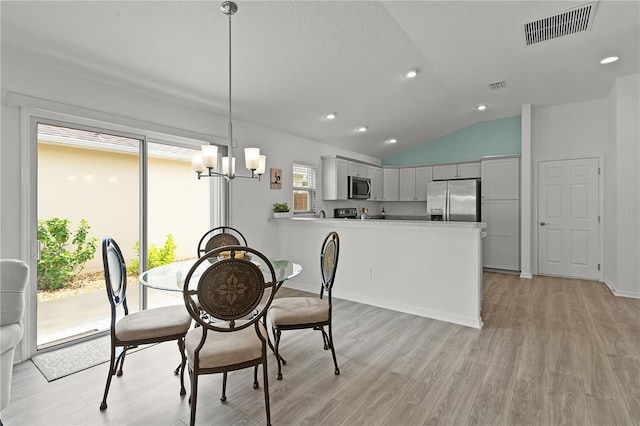 dining space featuring an inviting chandelier, a textured ceiling, light wood-type flooring, and vaulted ceiling