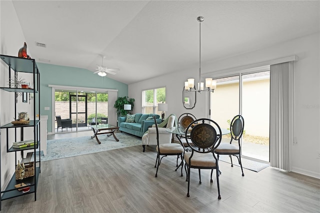 dining room with vaulted ceiling, ceiling fan with notable chandelier, and light hardwood / wood-style floors