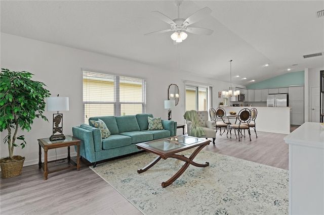 living room featuring lofted ceiling, light wood-type flooring, and ceiling fan with notable chandelier