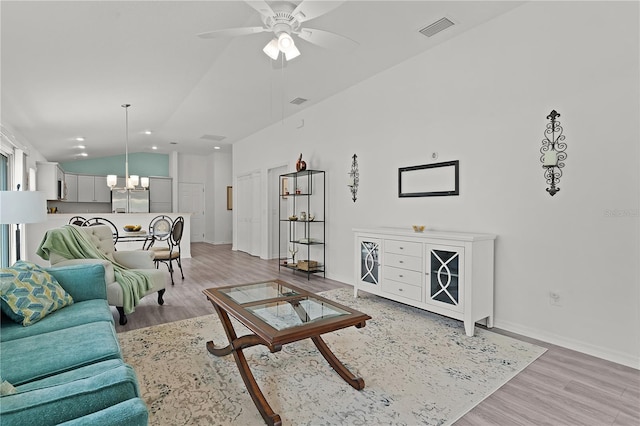 living room featuring lofted ceiling, ceiling fan with notable chandelier, and light wood-type flooring