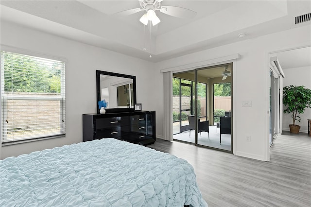 bedroom featuring access to exterior, wood-type flooring, a raised ceiling, and ceiling fan