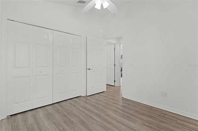 unfurnished bedroom featuring a towering ceiling, light wood-type flooring, a closet, and ceiling fan