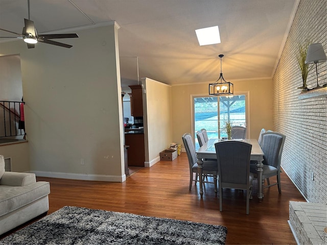 dining area featuring wood-type flooring, ornamental molding, a skylight, ceiling fan with notable chandelier, and brick wall