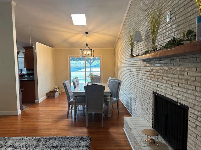 dining space featuring an inviting chandelier, ornamental molding, dark wood-type flooring, and a brick fireplace