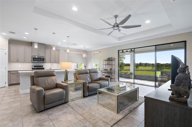 living room with ceiling fan, a tray ceiling, and light tile patterned floors