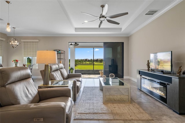 tiled living room with a raised ceiling and ceiling fan with notable chandelier