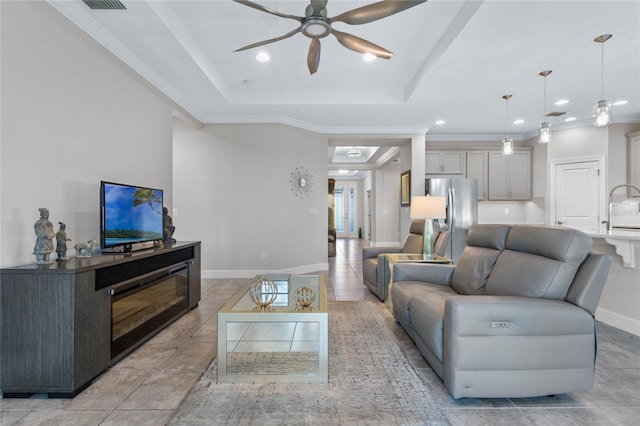 tiled living room with a tray ceiling, ceiling fan, ornamental molding, and sink