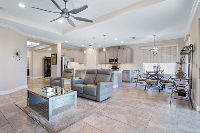 tiled living room featuring sink, crown molding, ceiling fan with notable chandelier, and a raised ceiling