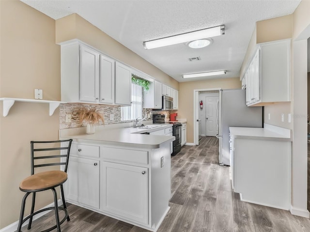 kitchen featuring light countertops, visible vents, a peninsula, stainless steel appliances, and white cabinetry