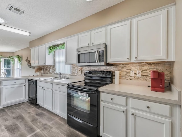 kitchen with a sink, visible vents, white cabinetry, and black appliances
