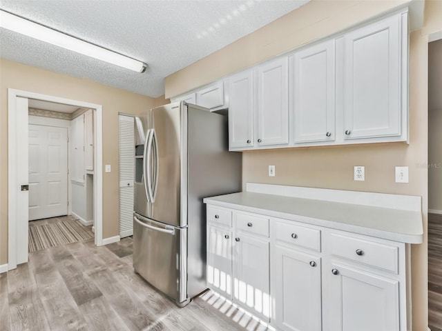 kitchen featuring light wood-type flooring, white cabinets, a textured ceiling, and stainless steel fridge