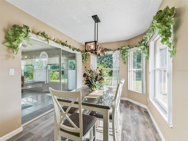 dining area featuring a textured ceiling, wood finished floors, baseboards, and a chandelier