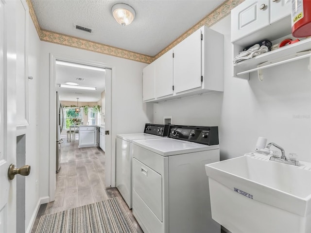 laundry room featuring a textured ceiling, cabinets, washer and clothes dryer, sink, and light hardwood / wood-style flooring