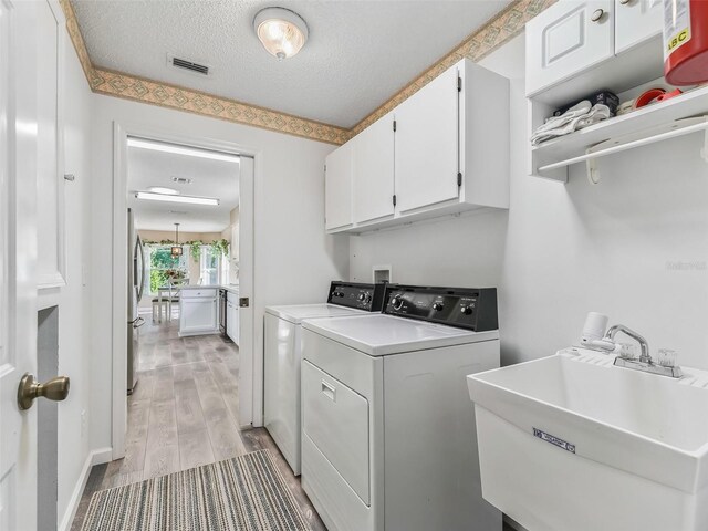 clothes washing area with light wood-type flooring, a sink, visible vents, cabinet space, and washing machine and dryer