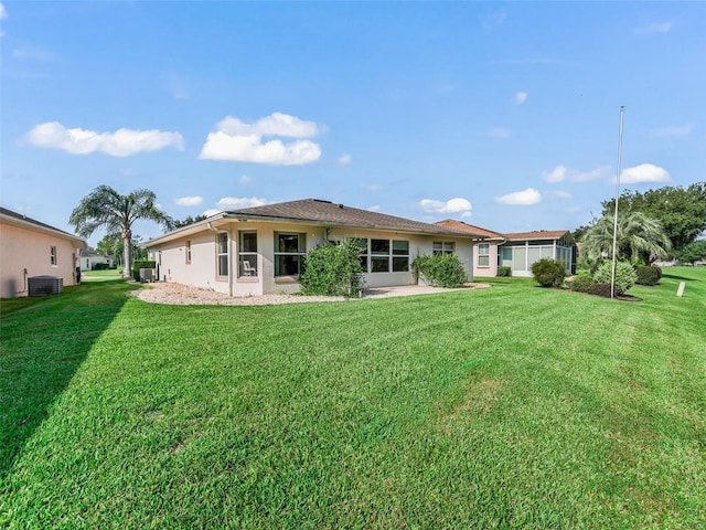 rear view of house with central air condition unit, a lawn, and stucco siding